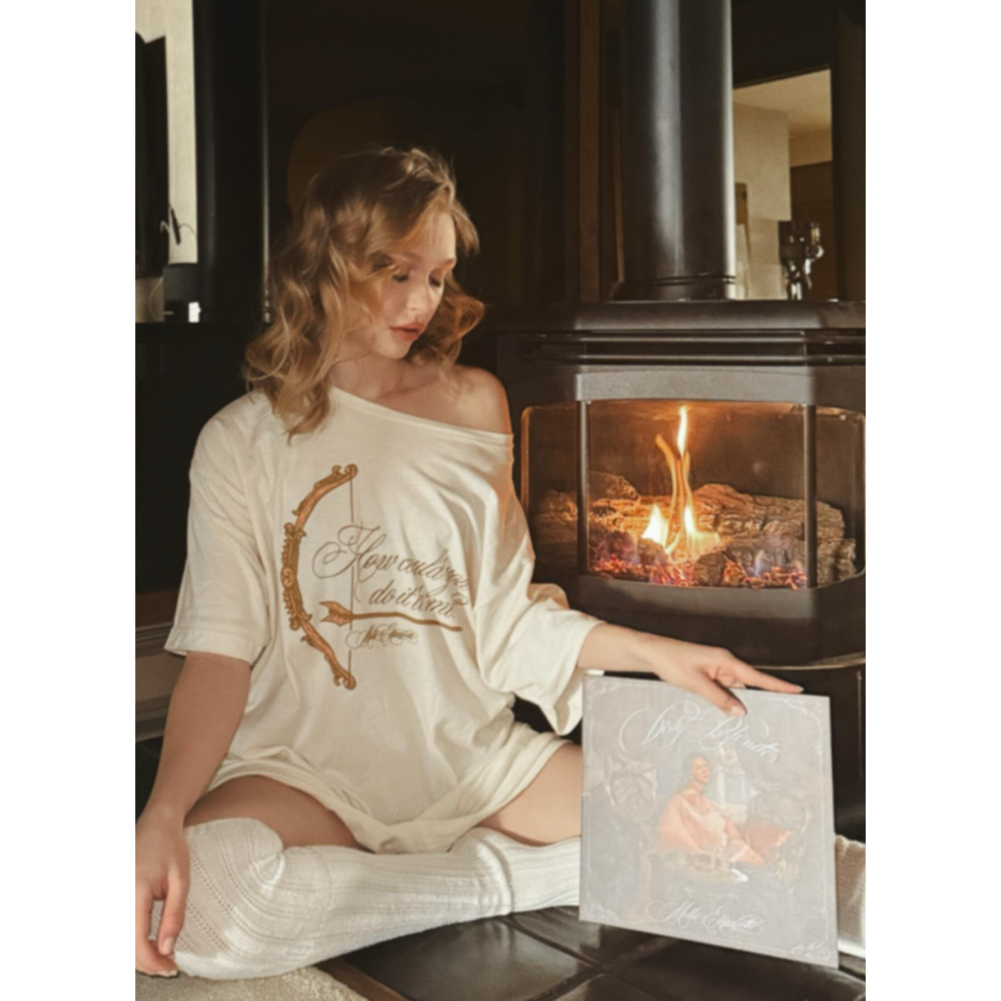 Mollie Elizabeth sitting by a fireplace wearing the Arrow Tee
