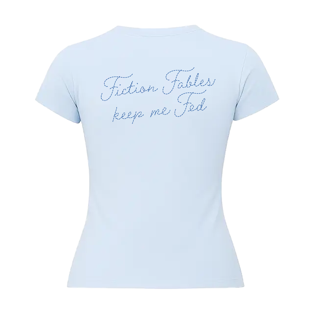 A light blue short-sleeve baby t-shirt shown from the back, featuring the phrase 'Fiction Fables keep me Fed' printed in a blue cursive script across the upper back.