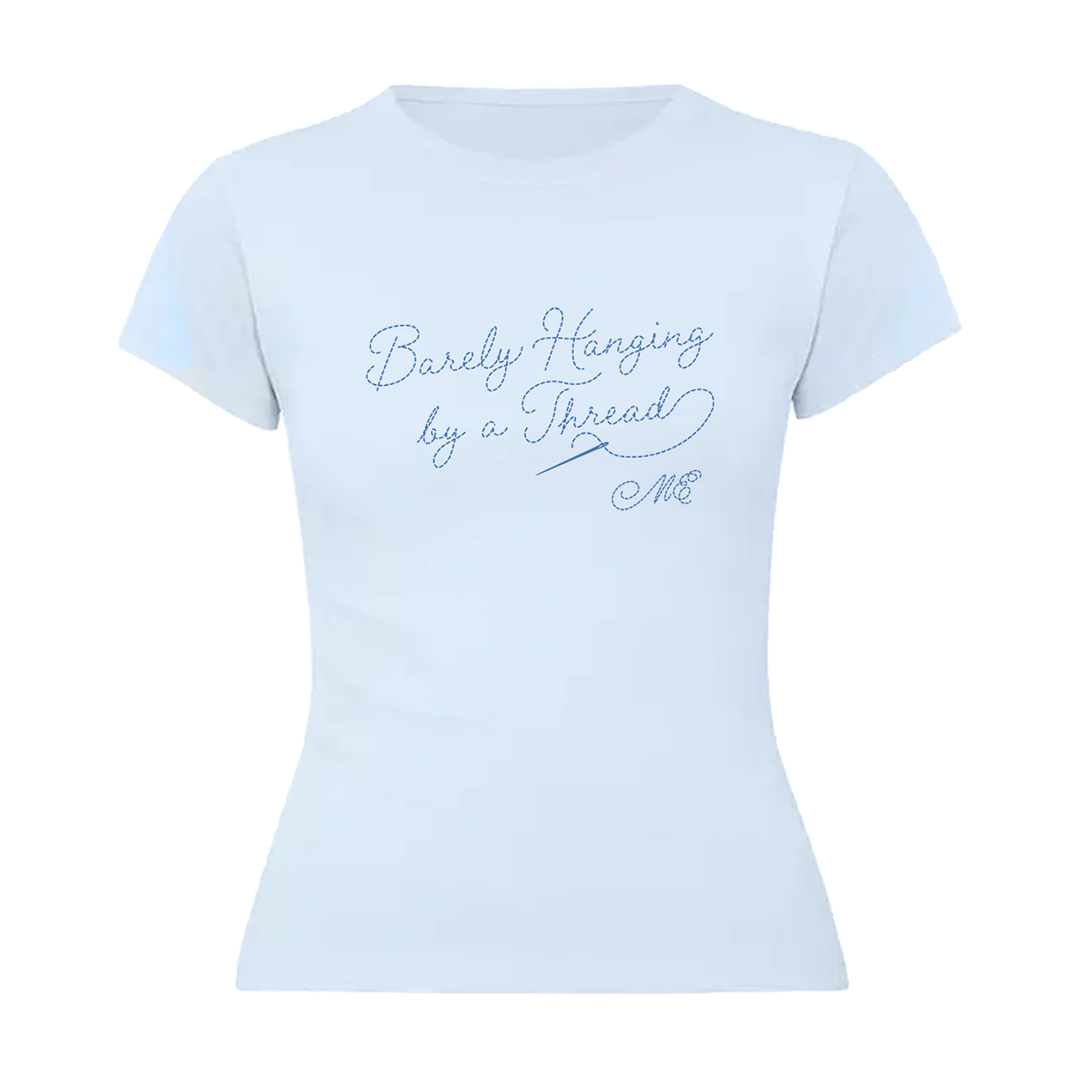 A light blue short-sleeve baby t-shirt with blue cursive text reading 'Barely Hanging by a Thread' and 'M&E' on the front in a threaded typography