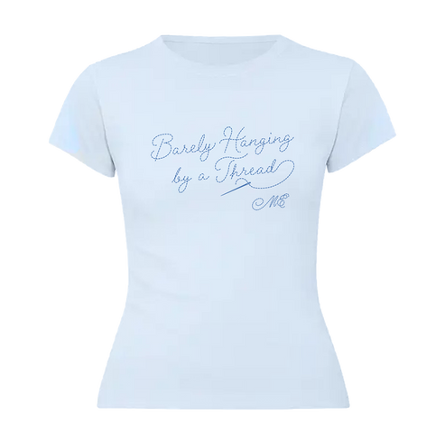 A light blue short-sleeve baby t-shirt with blue cursive text reading 'Barely Hanging by a Thread' and 'M&E' on the front in a threaded typography